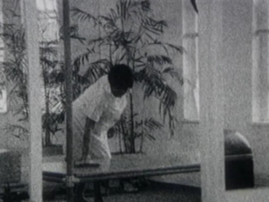 A black and white image of a black woman cleaning a bench in a gym.
