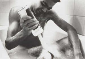 A young man sits in a bath while pouring a white powder onto his leg.