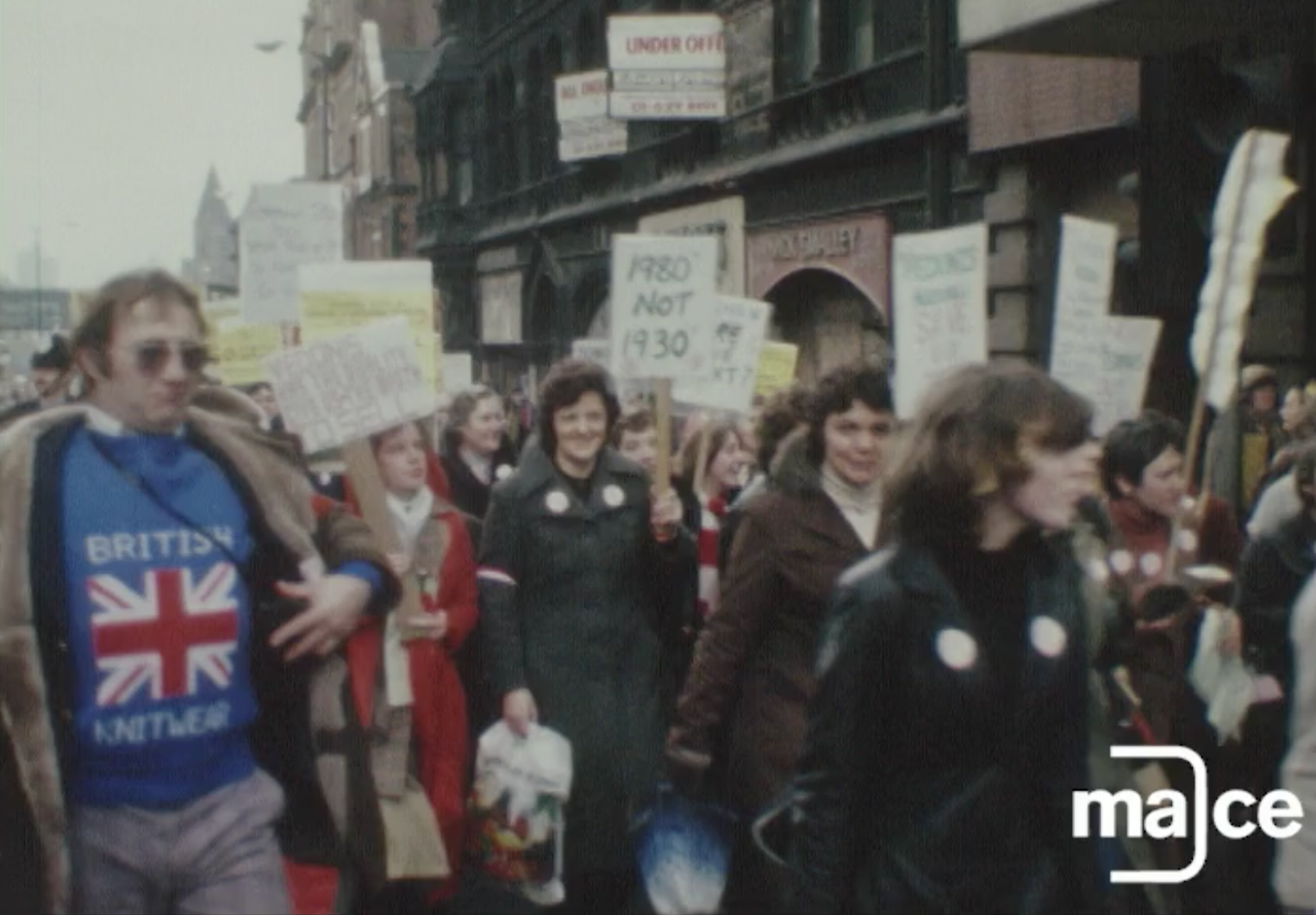 An archive film still showing a crowd of protestors walking down a city street.