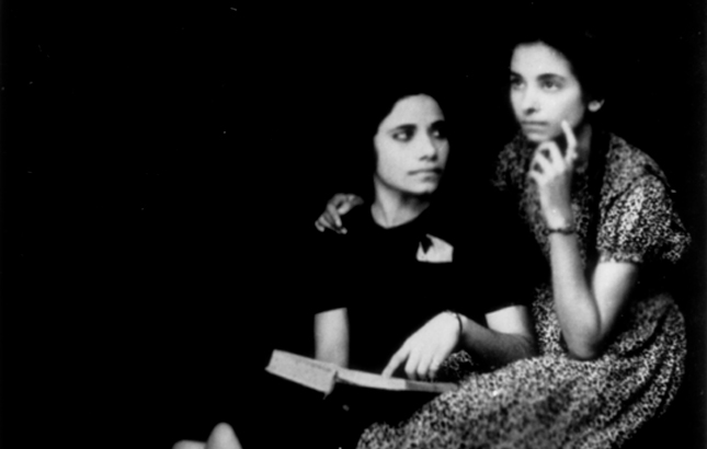 In black and white, two adolescent girls sit side by side and contemplating an open book.