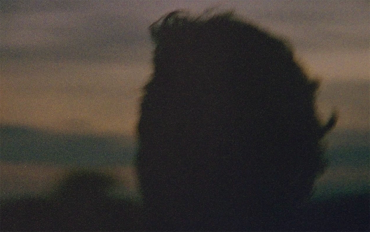 A person's head silhouetted against a dark horizon at sunset. Their hair stands up in the wind.